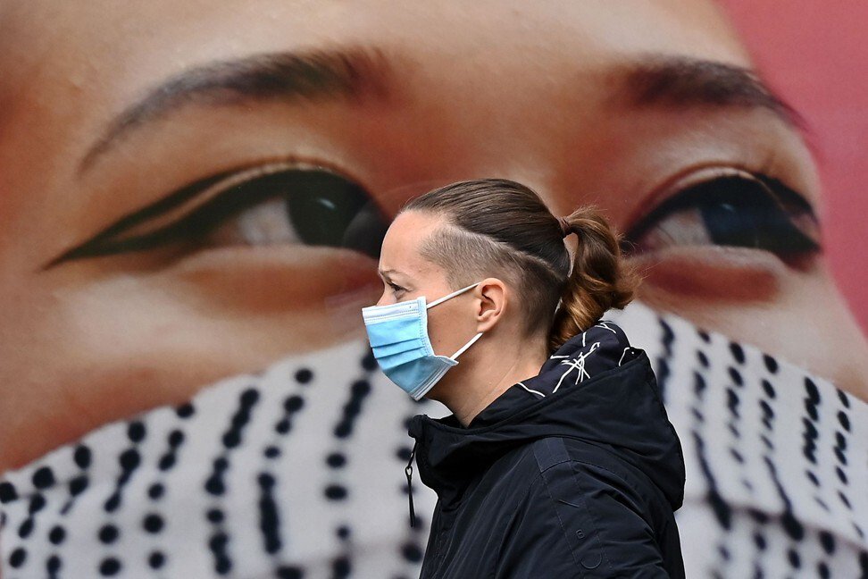 Тканинна маска на плакаті, медична на людині перед плакатом. Фото: AFP