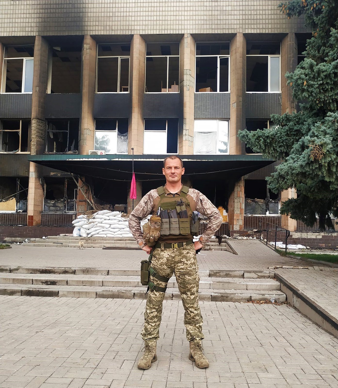 Автор на тлі спаленої будівлі мерії (будівля постраждала від обстрілів російської армії)
