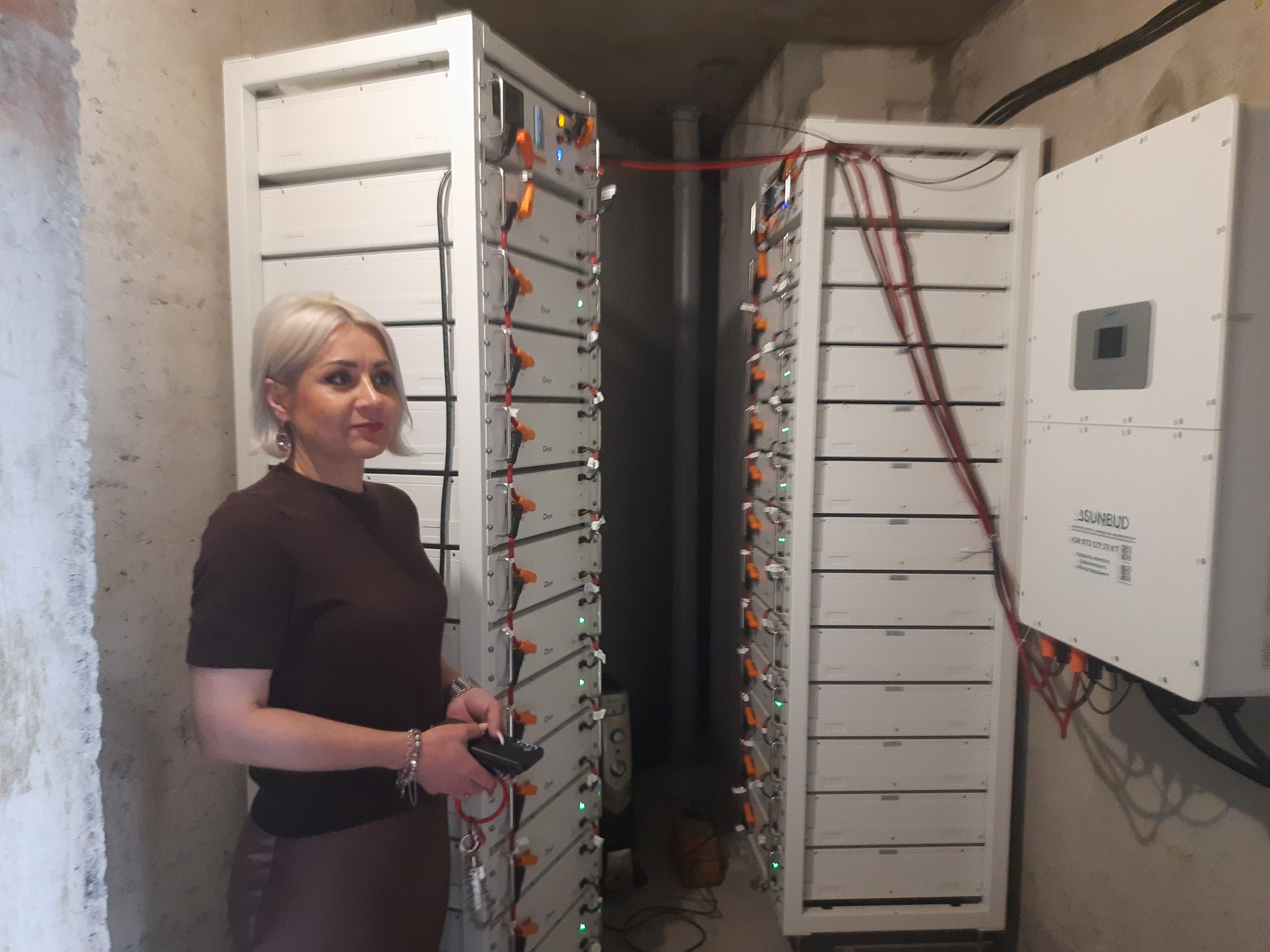 Вікторія Шмегельська показує будинкові акумулятори та інвертор (висить на стіні). Завдяки цьому обладнанню ліфти працюють під час відключень центрального електропостачання