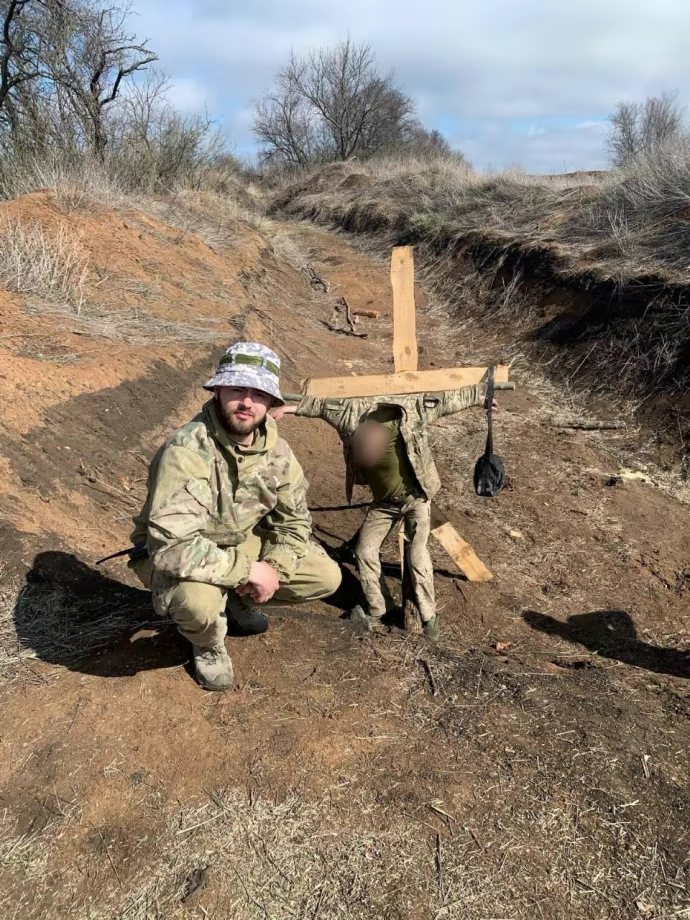 Владислав Пастух фотографується на тлі прив'язаного до хреста військовослужбовця