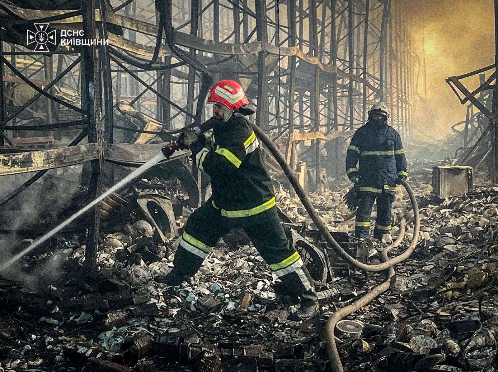 Рятувальники ліквідовують пожежу, що виникли внаслідок російської атаки БпЛА на Київщину 12 серпня. Судячи з вигорілих стелажів на фото, йдеться про великий маркет або логістичний центр
